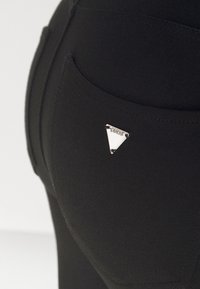 Svarta leggings med en silverfärgad triangulär logotags på bakfickan, tillverkade av ett elastiskt, sl ätt material med en åtsittande design.