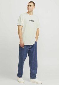Kortærmet crème t-shirt med "ART MODERNE" i sort tekst, parret med blå løstsiddende jeans og hvide sneakers. Enkelt design og afslappet pasform.