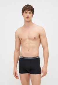 Melnas boksa bikses, kas izgatavotas no mīksta auduma, ar ērtu jostasvietu, kas rotāta ar baltām svītrām. Aizsargājošs dizains ar vidēja pacēluma griezumu.