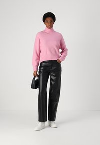 Rosa Rollkragensweater mit lockerer Passform, kombiniert mit schwarzen Kunstlederhosen, weißen Sneakers und einer kleinen schwarzen Handtasche.