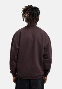 Dark purple sweatshirt with a relaxed fit, dropped shoulders, and ribbed cuffs. Fabric appears soft with a smooth texture.