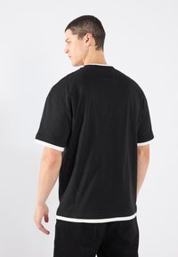 Tricou din bumbac negru cu mâneci scurte, având accente albe pe guler și marginea mânecilor. Croială lejeră și design clasic cu guler rotund.