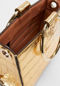 Borsa a tracolla oro con stampa coccodrillo, dotata di hardware circolare dorato e un interno marrone con fessure per carte e una texture in pelle liscia.