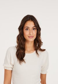 Lys beige ribbet top med korte pufærmer og en rund halsudskæring. Stoffet har en struktureret finish og en tætsiddende silhuet.