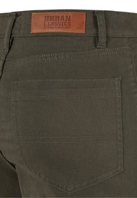 Pantaloni di cotone verde scuro con un patch in pelle etichettato "URBAN CLASSICS" e dettagli a doppia cucitura sulla tasca posteriore.