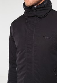 Czarna pikowana kurtka z wysokim kołnierzem i zapięciem na zamek. Posiada subtelne logo na piersi oraz boczne kieszenie na zamek. Gładka faktura.