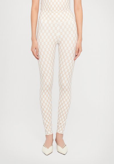 Leggings blancs ornés d'un motif géométrique répétitif en marron clair. Coupe ajustée avec une texture lisse, assortis à des chaussures blanches pointues.