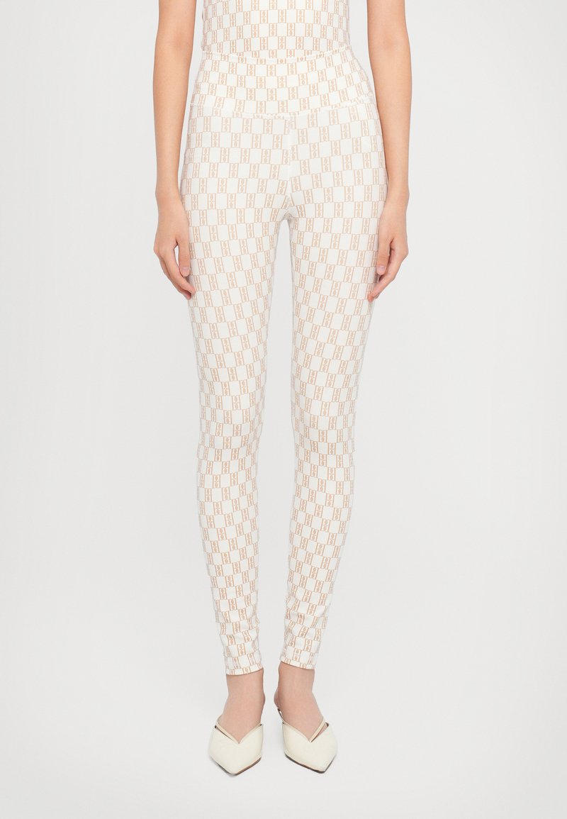 Witte leggings met een herhalend geometrisch patroon in lichtbruin. Strak aansluitende vorm met een gladde textuur, gestyled met puntige witte schoenen.
