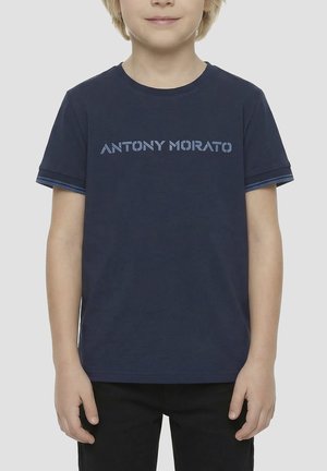 Bambino che indossa una maglietta blu navy con la scritta "ANTONY MORATO" sul petto e pantaloni neri su uno sfondo grigio chiaro.