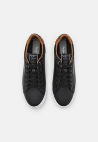 Czarne skórzane trampki z białymi podeszwami, z brązowymi akcentami na kołnierzu i czarnymi sznurowadłami. Widoczne logo na językach.