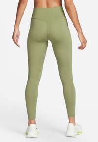 Vysoké, olivově zelené legíny z elastického materiálu s hladkou texturou a zúženými nohavicemi, doplněné bílými sportovními botami.