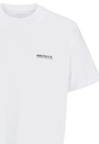 T-shirt en coton blanc avec col rond, manches courtes et un logo imprimé noir "ORIGINALS ST." sur la zone de la poitrine gauche.