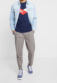 Denim button-up shirt, navy graphic t-shirt with red and white design, gray checkered trousers, blue sneakers with white accents.