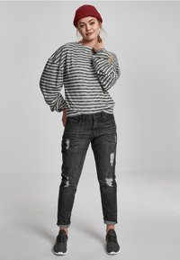 Grau-weißer gestreifter Langarmshirt, schwarze ausgewaschene Jeans und schwarze Sportschuhe. Das Modell trägt eine rote Strickmütze.