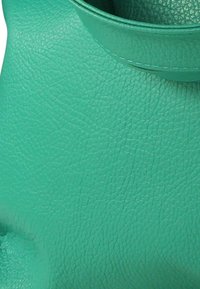 Turkooizen handtas van getextureerd leer met een afgeronde bovenkant en opvallende stiksels. Heeft een zachte, gladde afwerking en een minimalistisch ontwerp.