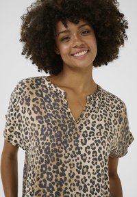 Blus med leopardmönster som har V-ringning, korta ärmar och lös passform. Tyget har en mjuk yta med beige och svarta färgmönster.