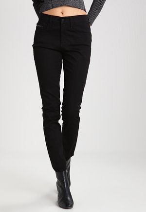 Persoon draagt hoge zwarte slim-fit broek en zwarte enkellaarzen, met een cropped grijze trui die de buik laat zien.