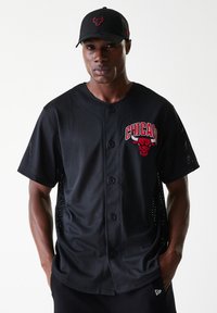 Black mesh baseball jersey with Chicago Bulls logo in red. Features buttons and short sleeves with perforated sides for breathability. Black cap.