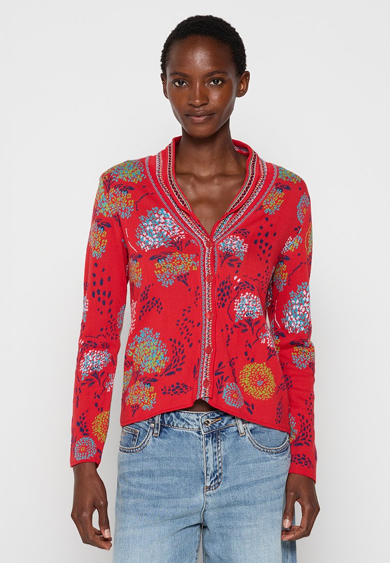 Czerwony kardigan z kwiecistym wzorem w kolorze niebieskim, żółtym i białym. Ma dekolt w serek, długie rękawy oraz zapięcie na guziki. Wykonany z teksturowanej przędzy.