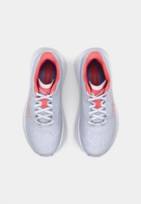 Baskets de sport gris clair avec une tige texturée, des lacets blancs et des accents roses autour du col et de la languette. Présente le logo HOKA.