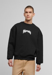 Zwarte sweatshirt met een oversized ontwerp, voorzien van witte geborduurde tekst op de borst. Gemaakt van zachte stof met ribgebreide manchetten en zoom.