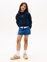 Felpa blu navy, in tessuto morbido, con logo. Abbinata a una mini gonna di jeans, sneakers beige chiaro e calzini bianchi alla caviglia.