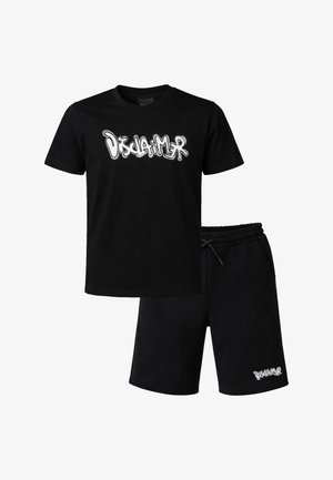 Outfit casual nero con testo "Disclaimer" in stile graffiti bianco sul petto della t-shirt e vicino all'orlo dei pantaloncini.