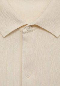 Cream-colored knitted polo shirt featuring a ribbed texture, two button closure, and a classic collar design.