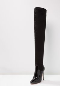 Stivale nero alti fino alla coscia, con punta in pelle verniciata lucida, alza in suede opaco, design a punta e tacco a stiletto.