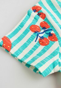 Tyrkysovo-bielo pruhovaná látka s červenými usmievajúcimi sa ilustráciami čerešní, spojených modrými stopkami, zložená na bledom povrchu.