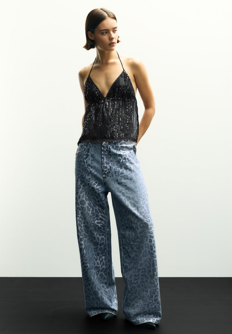 Sort paillet halterneck-top med en dyb udskæring, parret med lyseblå, brede jeans med leopardmønster.