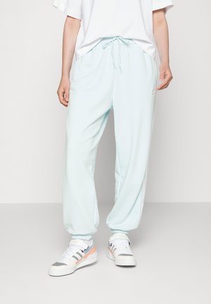 Osoba nosząca jasnoniebieskie spodnie dresowe z elastycznymi ściągaczami i białą koszulkę, w połączeniu z białymi sportowymi butami z różowymi i szarymi akcentami.