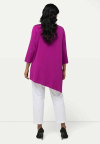 Magenta, asymmetrische Tunika mit dreiviertel Ärmeln, kombiniert mit weißen Hosen und schwarzen High-Heels. Glatte Textur, schlichtes Design.