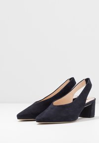 Slingback boty v námořnické semišové kůži s špičatou špičkou a blokovým podpatkem. Mají otevřenou zadní část a výřezový design na bocích.