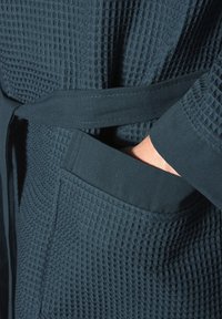Dark teal waffle-textured robe with a fabric belt and deep pockets. Features ribbed cuffs and a soft finish, emphasizing comfort and practicality.