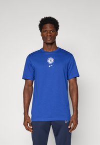 Blå bomulds t-shirt med korte ærmer, prydet med et cirkulært Chelsea FC emblem og Nike logo på brystet. Glat tekstur og rund hals design.