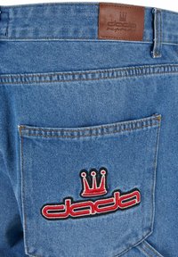 Blaue Denim-Jeans mit einem Lederetikett am Bund. Die Gesäßtasche verfügt über ein rot und schwarz gesticktes Logo mit einem Kronendesign.