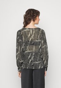 Blusa preta com padrões brancos ondulados, mangas longas e um pequeno detalhe em forma de chave nas costas. Tecido suave e leve. Combinada com calças escuras.