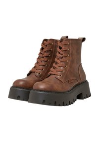 Brązowe botki na kostkę z ekologicznej skóry, związane sznurówkami, złotymi oczkami, wyściełanym kołnierzem i grubą czarną podeszwą na koturnie z ząbkowanym brzegiem.