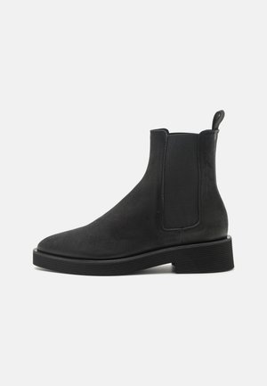 Bottines Chelsea en cuir noir avec des panneaux élastiques sur les côtés, bout arrondi et semelle en caoutchouc texturé. Équipées d'une languette à l'arrière pour un enfilage plus facile.
