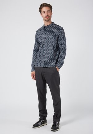 Chemise à manches longues bleu marine avec un motif géométrique, col ouvert, associée à un pantalon gris foncé et des baskets noires.