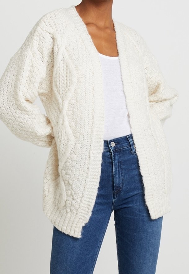 Texturerad vit stickad cardigan med en lös passform, som har ett kabelmönster fram och ribbade kanter. Bärs över en ljus topp och jeans.