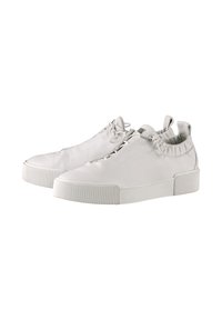 Para białych sneakersów niskich z elastycznymi kołnierzami na kostkę, sznurowaną frontem i grubymi gumowymi podeszwami na białym tle.