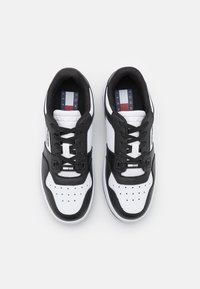 Sneakers bianchi e neri con superiore in pelle liscia, punta perforata, accenti neri a contrasto e solette marchiate visibili.