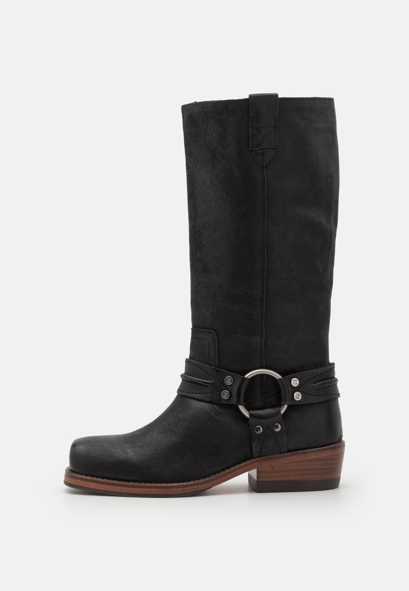 Black leather knee-high boot with a rounded toe, textured shaft, and decorative strap with a metallic ring. Block heel and sturdy sole.