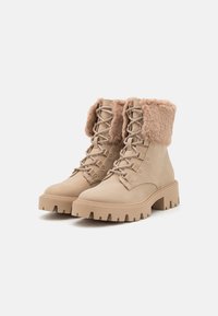 Bottes à lacets beiges à la cheville avec un col en fourrure douce, semelle en caoutchouc et talon épais ; en daim doux avec des détails texturés sur la tige.
