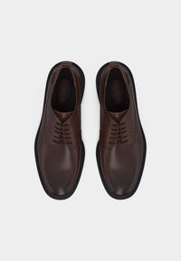 Paire de chaussures habillées en cuir marron foncé à lacets, semelles noires, vues de dessus sur fond blanc.