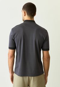 Kortærmet polo-shirt i mørkegrå med sort mønstret kant på krave og ærmer, lavet af glat stof og med en afslappet pasform.