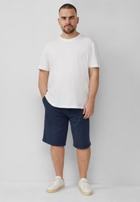 Witte katoenen t-shirt, marineblauwe shorts en witte sneakers met beige zolen. Eenvoudig ontwerp; geen zichtbare patronen of accenten.