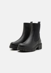 Bottes de cheville en cuir noir avec des panneaux élastiques sur les côtés, bout rond, talon bloc texturé et languettes à l'arrière pour un enfilage facile.